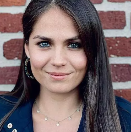 Kathy, dressed in business casual attire, is standing in front of a red brick wall. 